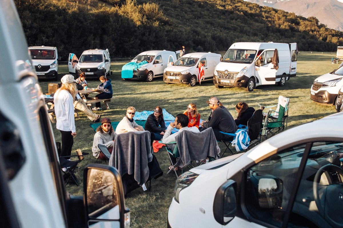People are sitting on chairs inside a circle of campervans