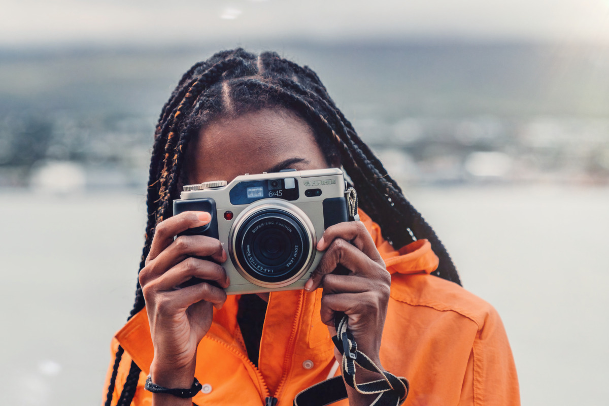 A woman in orange jacket is holding a camera