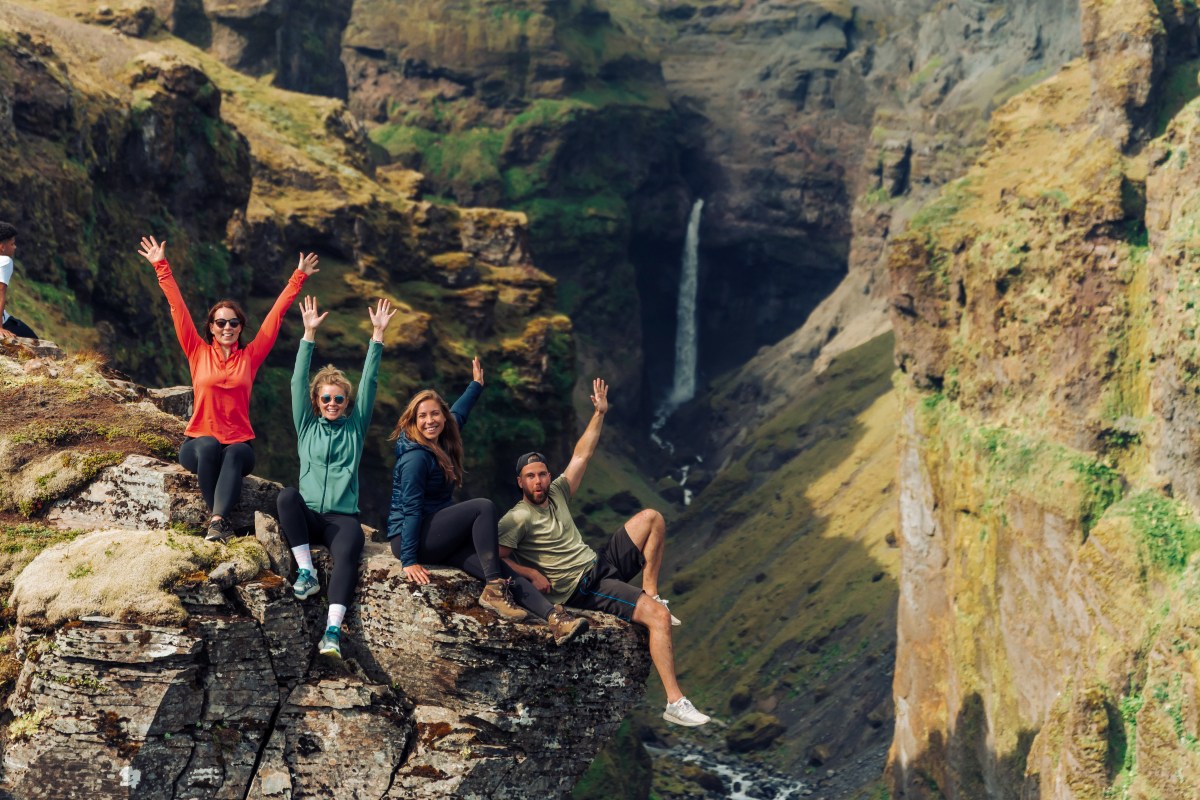 Four people are sitting on the rocks and are waving