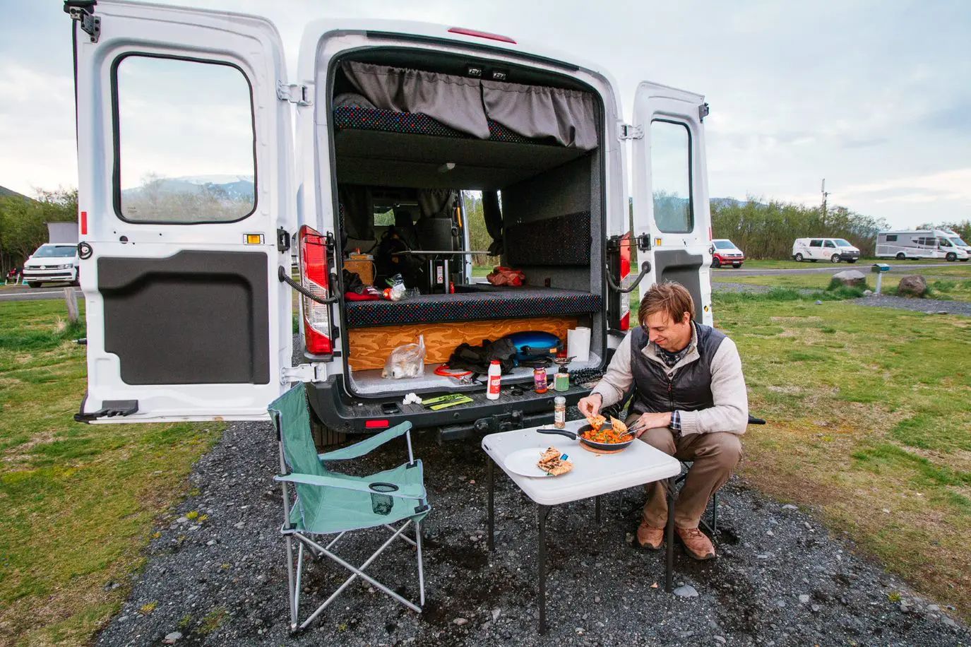 A man preparing food in the back of the camper van on the campsite