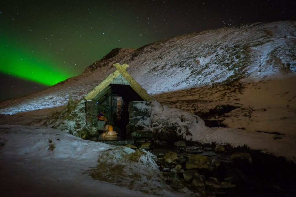 Hot spring during the winter with dancing northern lights above.