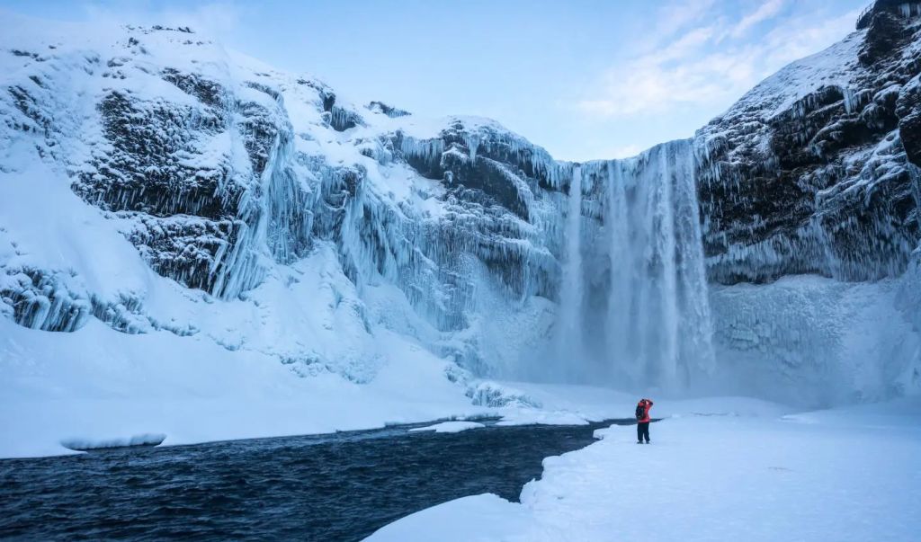 A man watching a frozen Skogafoss waterfall.