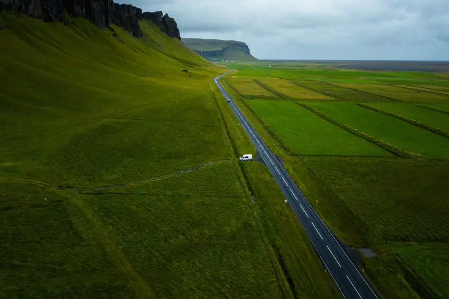 White campervan on the road in Iceland surrounded with grass and mountains.