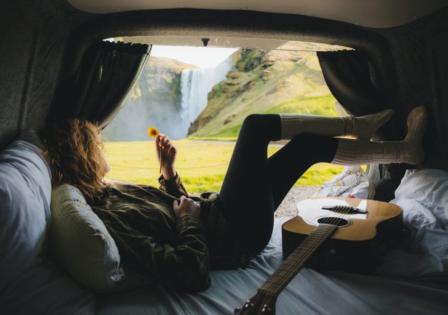 A woman is lying on the bed in the campervan and watching the waterfall.