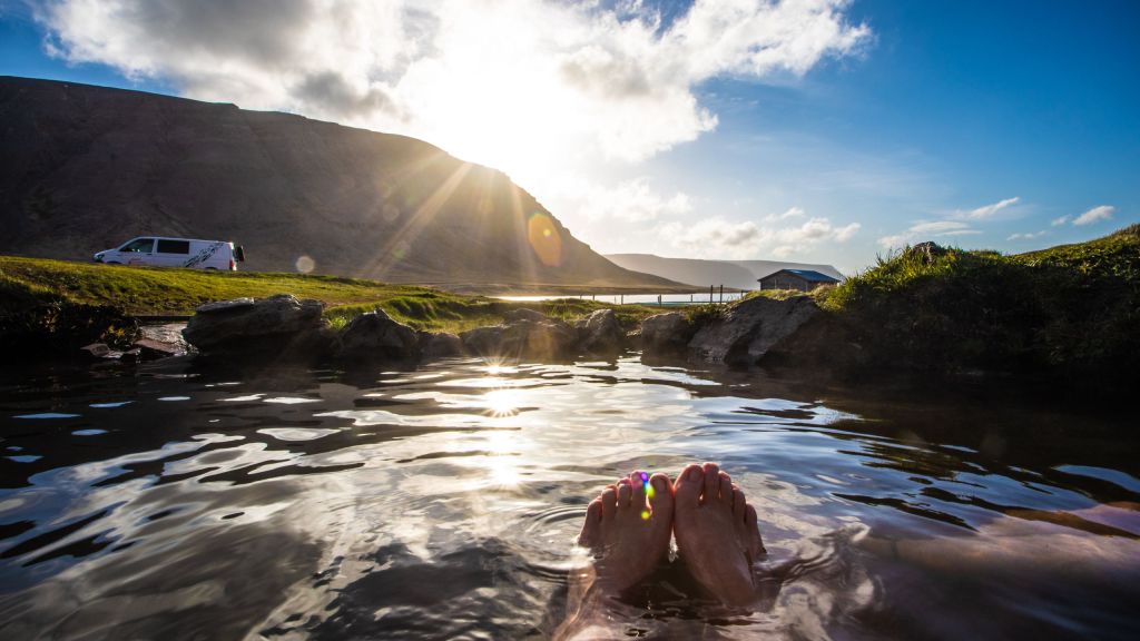 A man relaxing in the hot spring with a camper van and mountain in the background