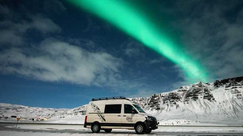 Campervan parked on the snow belowe Northern Lights
