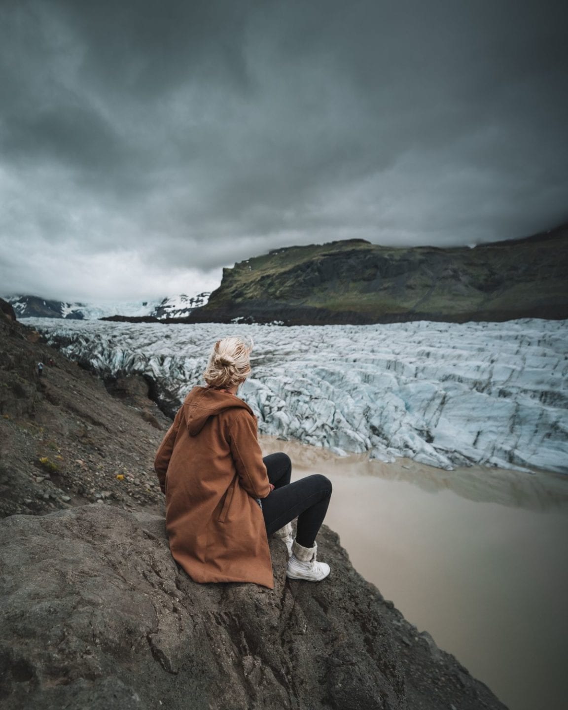 A woman sitting next to a glacier