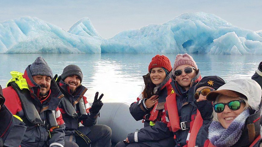 6 people smiling in a boat with glaciers in a background