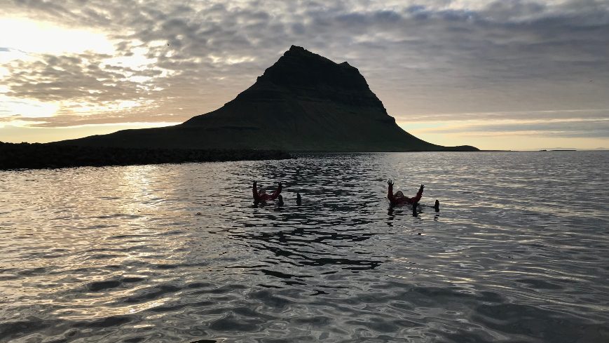 2 people swimming in a water with Kirkjufell in the background