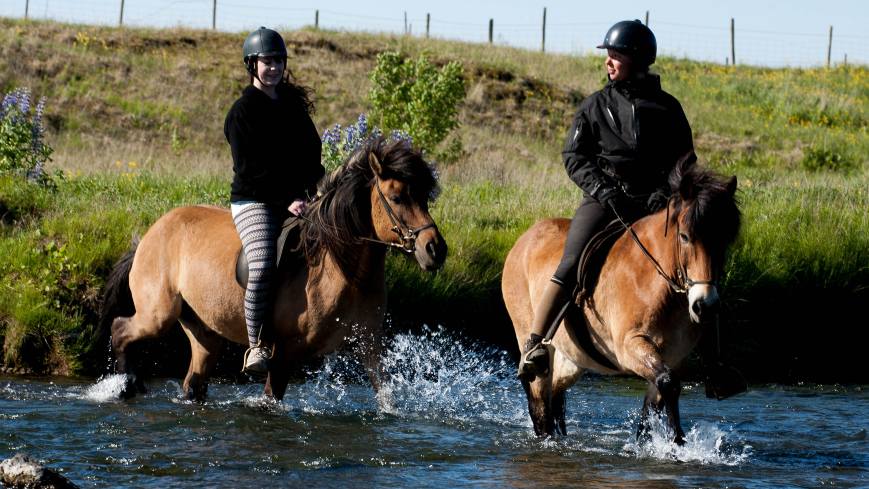 2 people are on their horseback riding tour. They are crossing a river