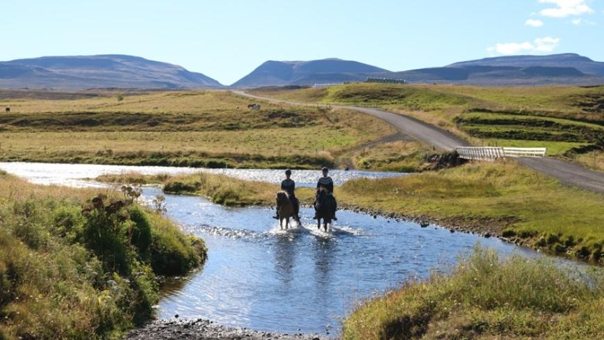 2 people are horseback riding across the river