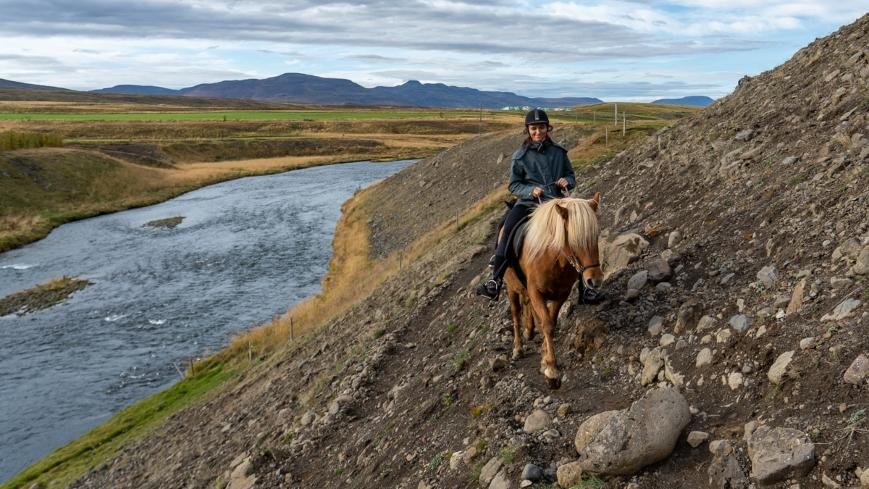A woman is riding o horse next to the river