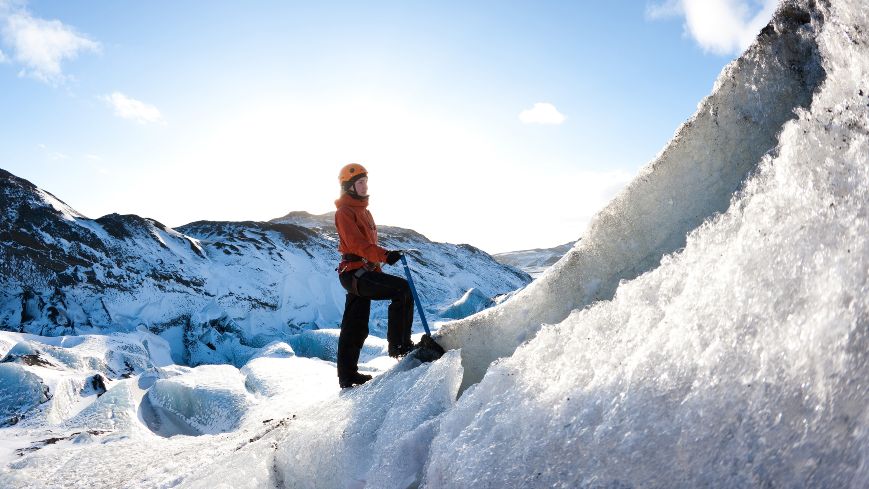 Woman is standing on the icy snow. There are the mountains in the background