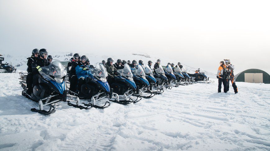 Group of people on snowmobiles are waiting to start their tour