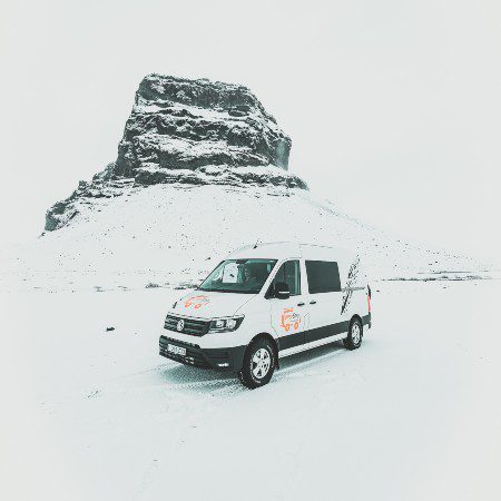 A camper van in snowy scenery. In the background there is a mountain