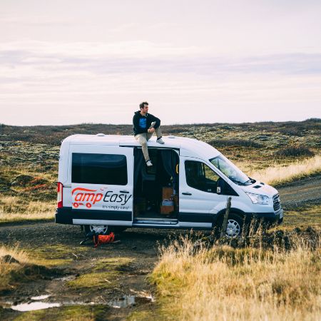 A man is sitting on the campervan surrounded by green scenery