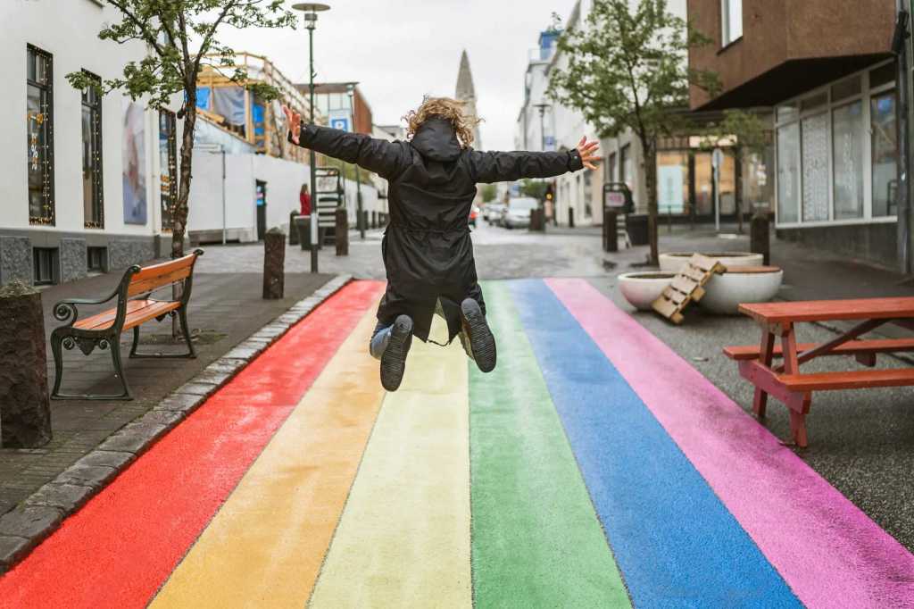 Anonymous boy jumping for joy in the streets of Reykjavik, Iceland on a roadway painted in the colours of the LGTBI+ rainbow flag.