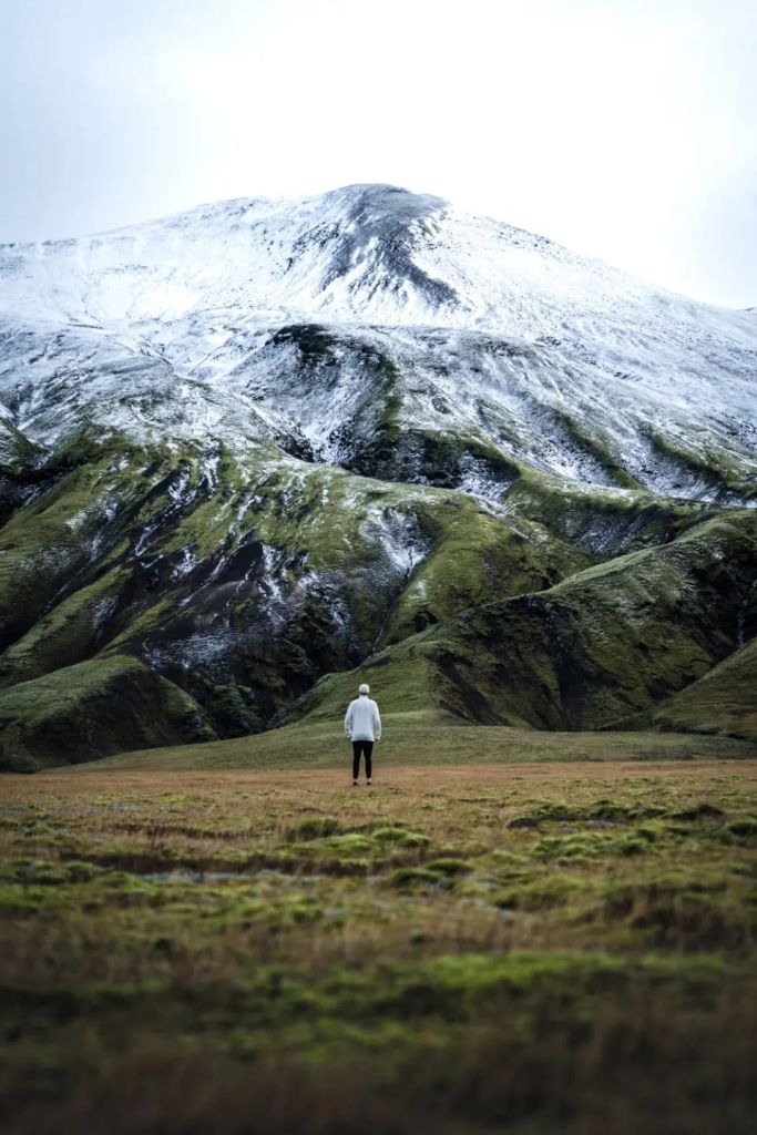 Man is standing in front of huge mountain covered by snow