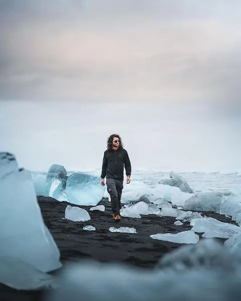 A man is walking through the icebergs on the black sand beach
