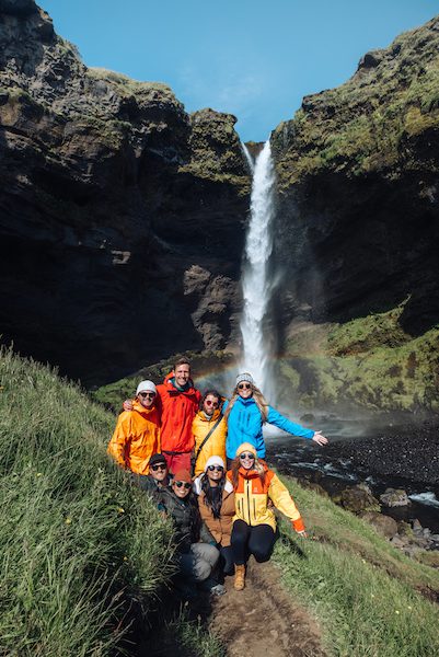 A group of people are standing in front of the waterfall