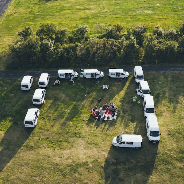 Group of people are sitting on the grass inside the circle of campervans