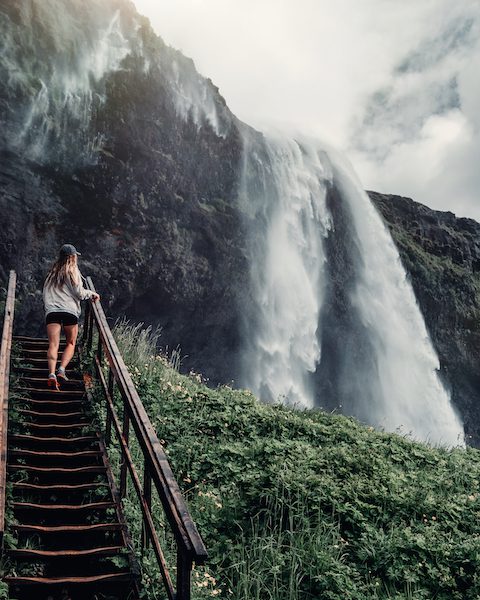 A woman is sanding on the stairs and watching the waterfall