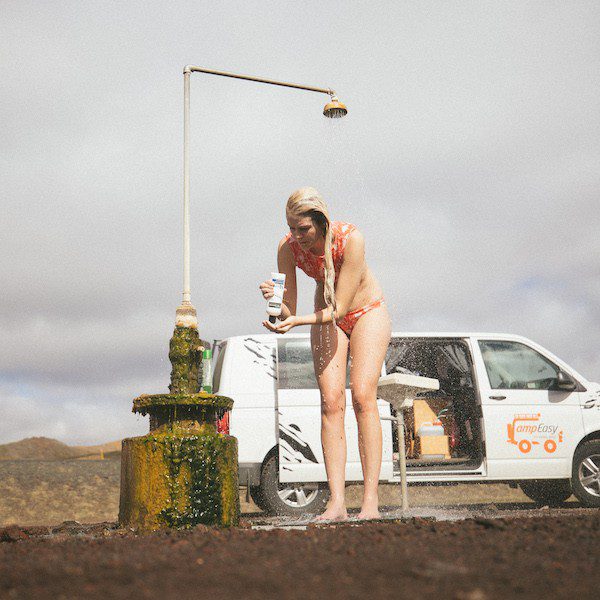 A woman in bikini is taking a shower in front of campervan