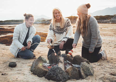 Three women are grilling food in a bonfire on the beach