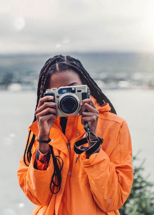 A woman in orange jacket is holding a camera