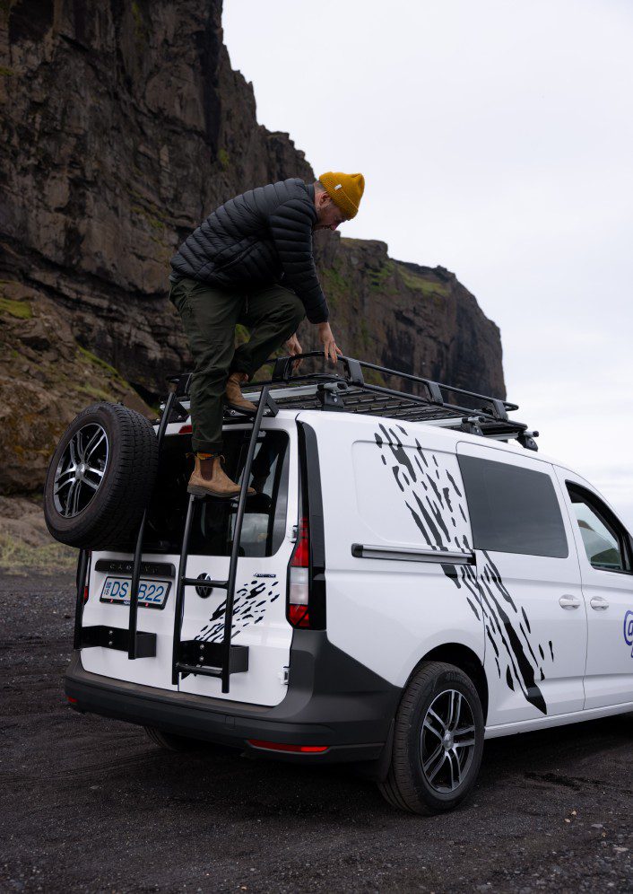Man is climbing the roof of the campervan.
