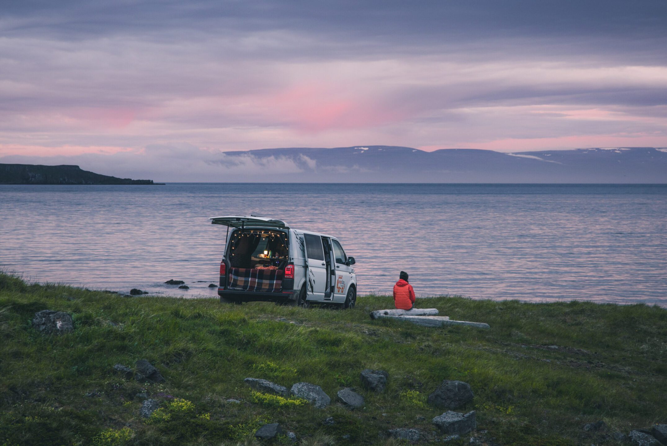 A person is sitting next to the campervan and looking at lake