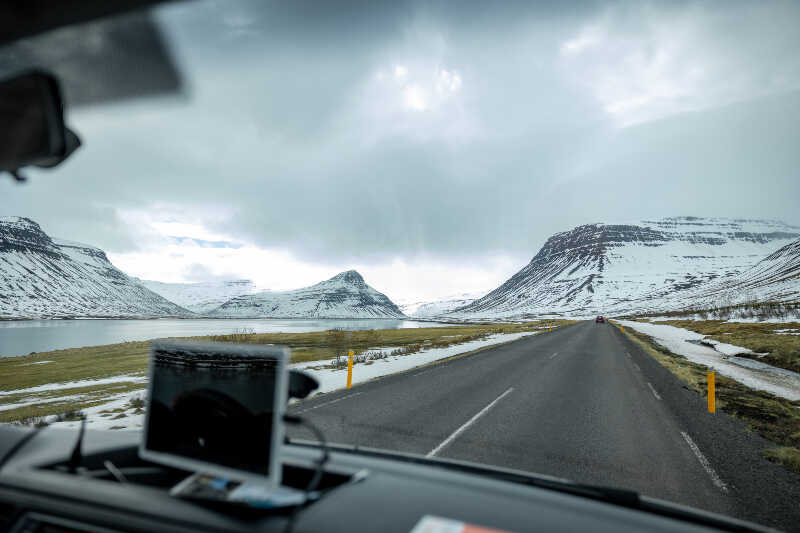 A view from front of the campervan on road, snowy mountains and a water