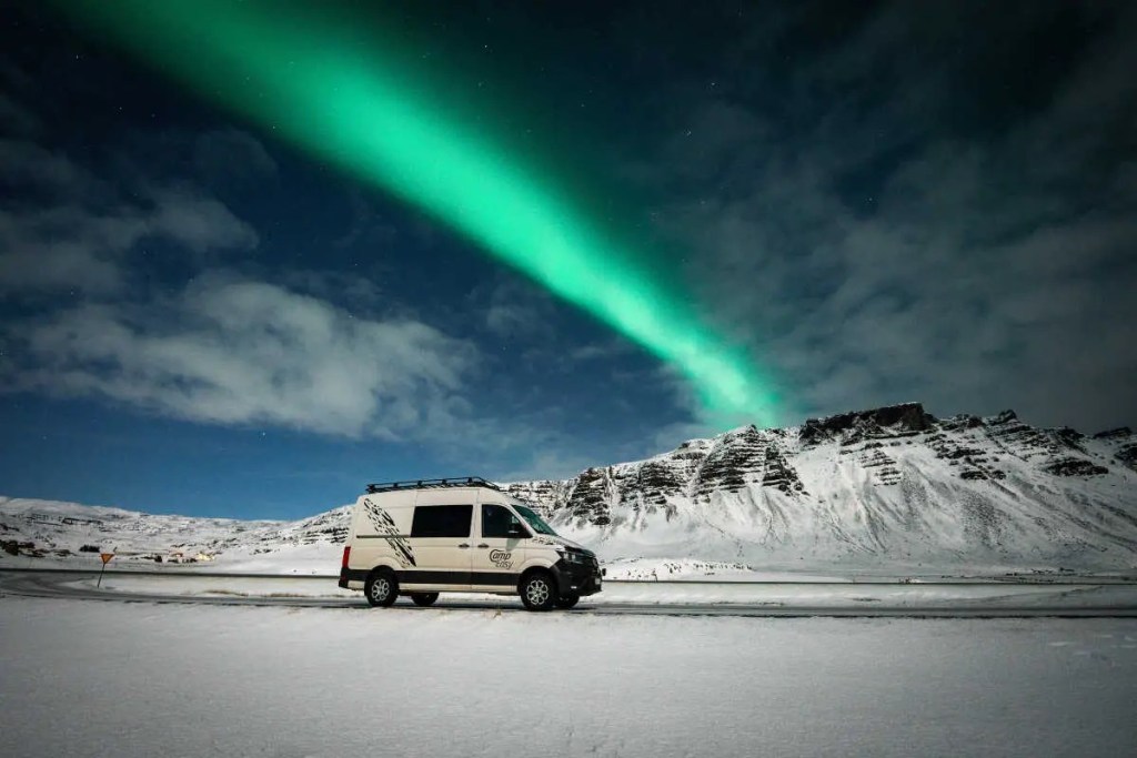 A campervan surrounded by winter landscape. There are the northern lights on the sky