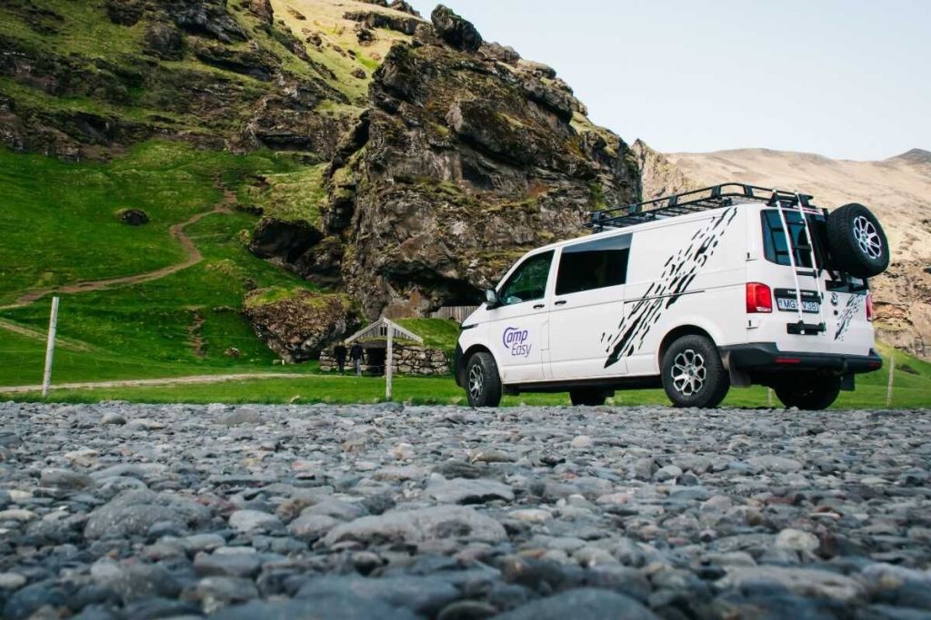 Camper van parked on the gravel next to the mountain and the old Icelandic house