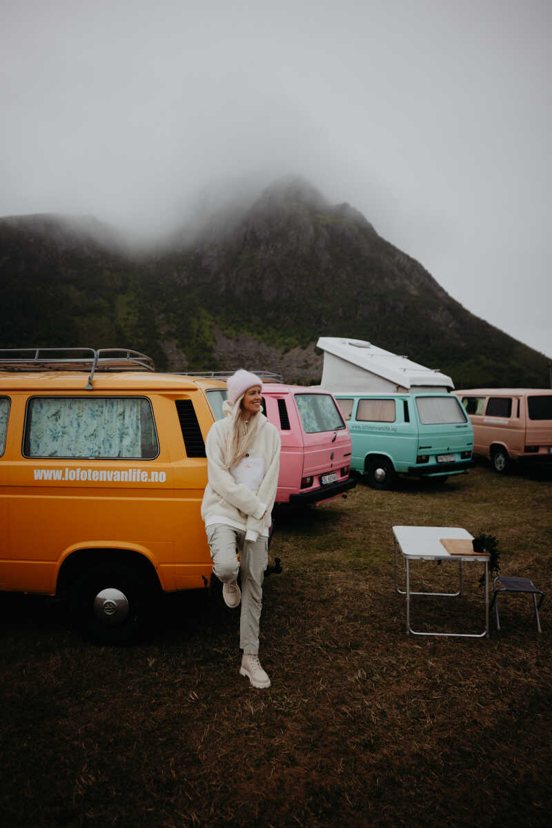 Two people are standing next to a campervan surrounded by a lupine field