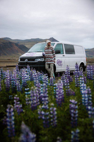 Woman standing next to the campervan surrounded by violet lupins