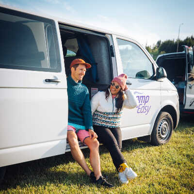 Two people are sitting on the side doors of the campervan