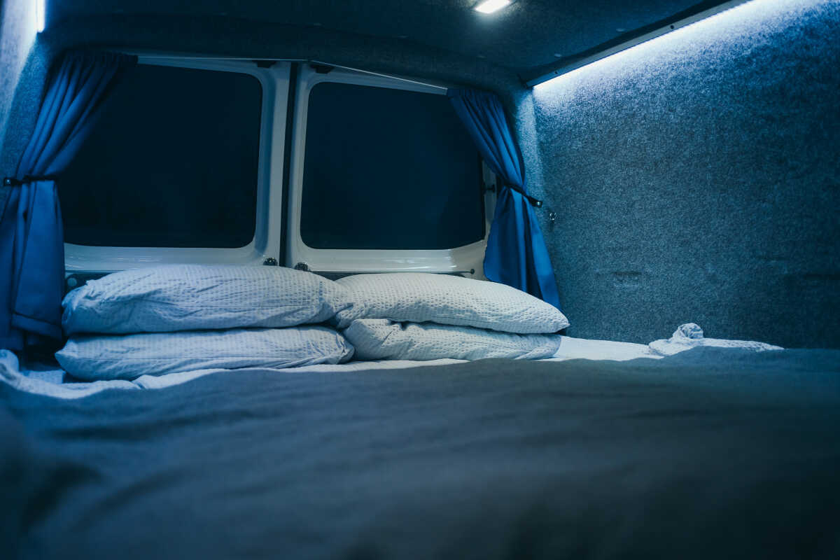 Interior view of the campervan focused on the sleeping area with already made bed