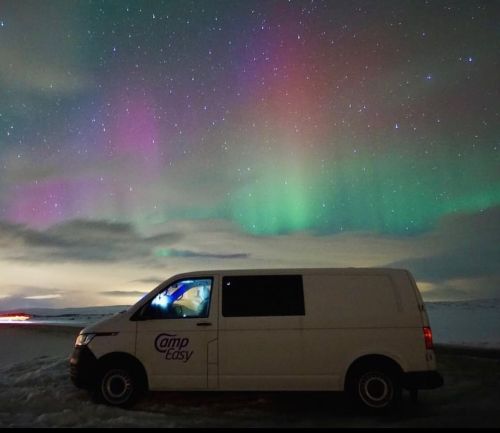 CampEasy camper van parked under a vibrant aurora display in a snowy landscape at night.