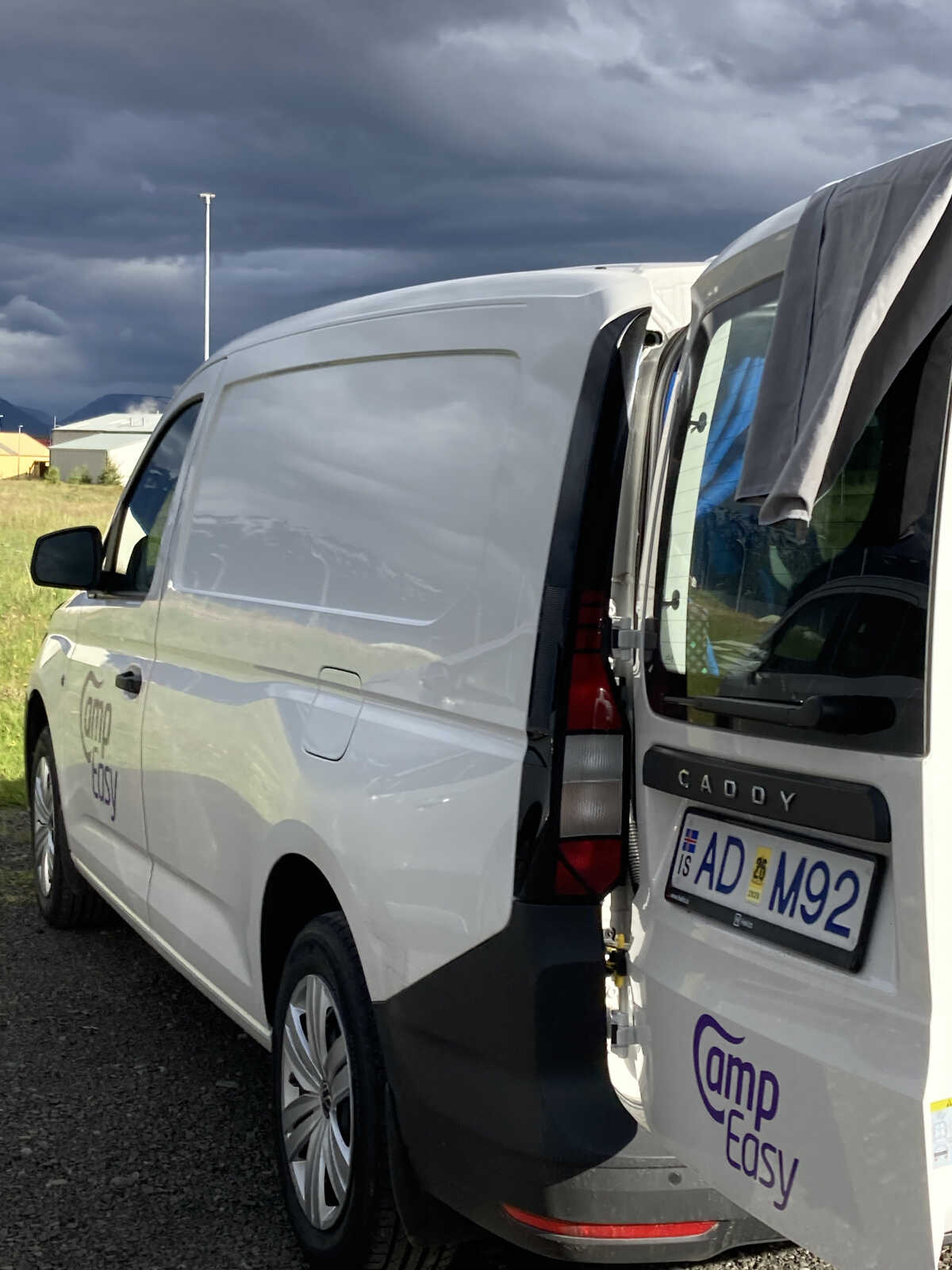 Camper van parked with doors open, under a stormy sky, highlighting the contrasting weather typical in Iceland.