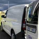 Camper van parked with doors open, under a stormy sky, highlighting the contrasting weather typical in Iceland.