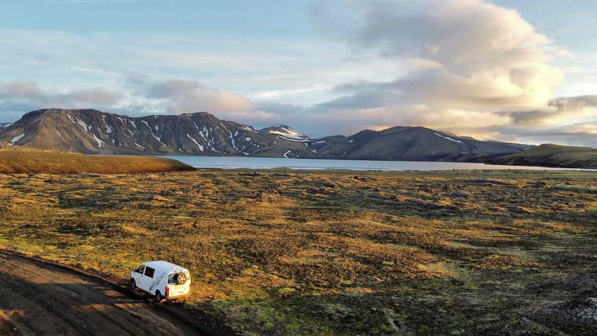 White Camp Easy camper van parked on a rugged road in the vast Icelandic highlands, with panoramic views of distant mountains and a serene lake.