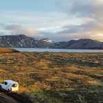 White Camp Easy camper van parked on a rugged road in the vast Icelandic highlands, with panoramic views of distant mountains and a serene lake.