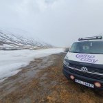 Front view of a CampEasy campervan parked beside a snowy road with a mountainous backdrop, emphasizing rugged terrain travel in Iceland.