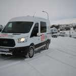 CampEasy campervan navigating through a snow-covered street in a small Icelandic town, with quaint houses and a snow-capped mountain in the background during a gray winter day