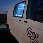 Nighttime view of a CampEasy campervan parked in a rugged Icelandic landscape, with a vibrant volcanic eruption glowing in the background, highlighting unique travel experiences in Iceland.