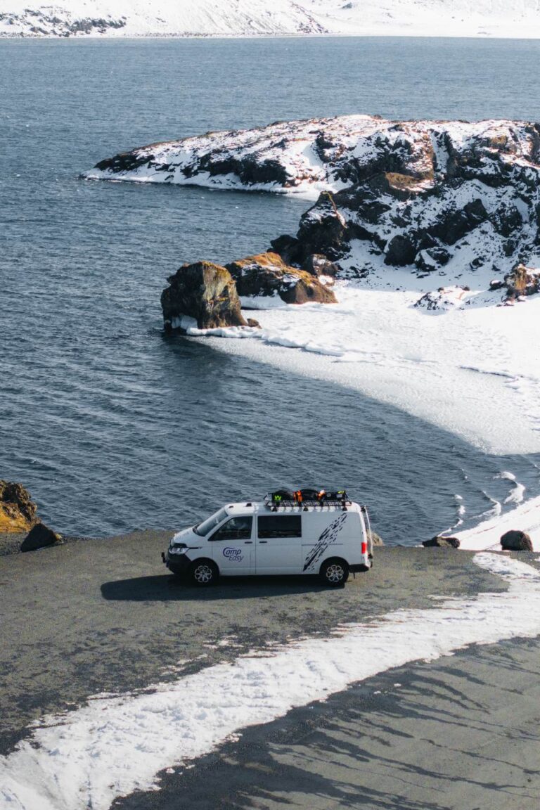 A campervan parked on the side of the road near the snow-covered shore of a fjord.