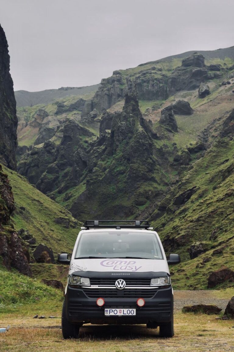 A camper parked on the grass near mountains covered with green grass and moss.