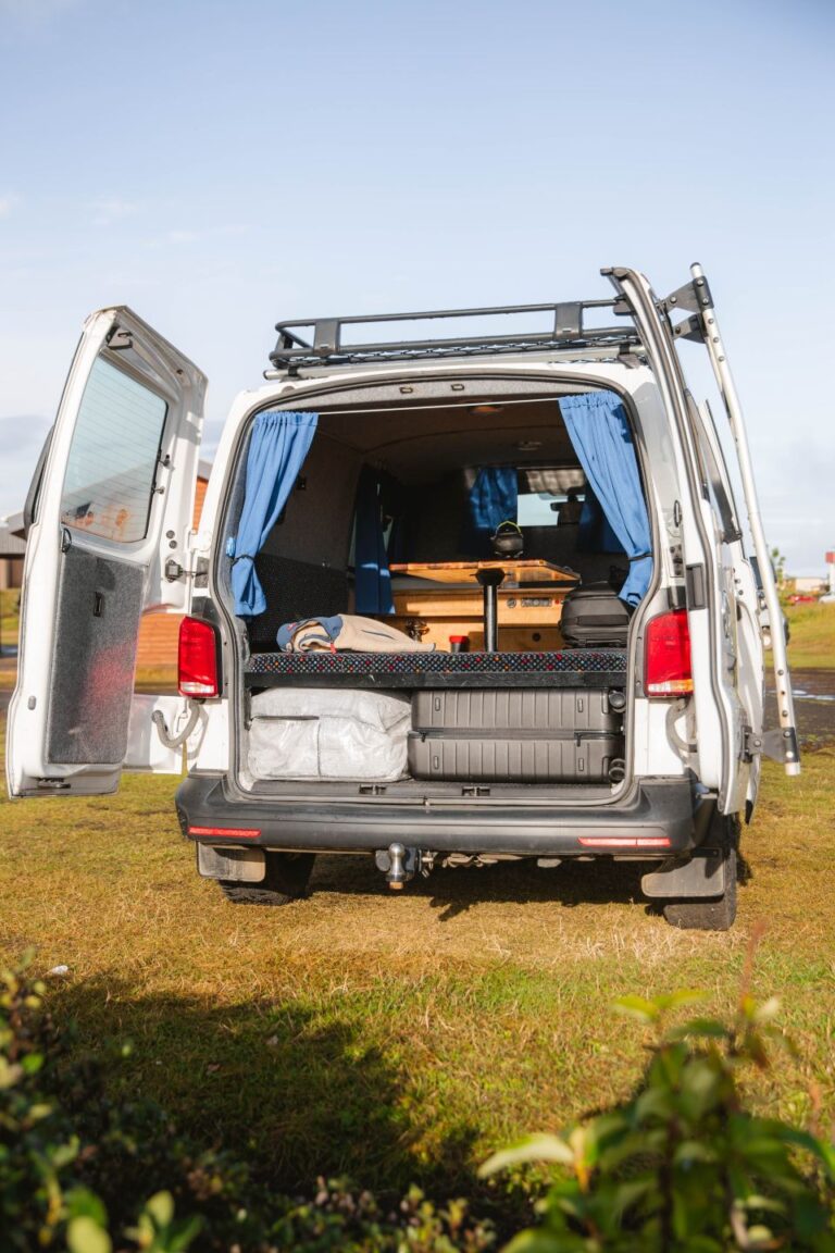 A camper van with its rear door open, parked at a campsite.