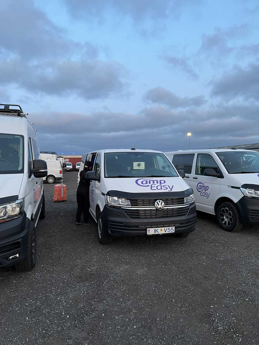 CampEasy Volkswagen campervans parked in a row at a rental facility during dusk, with a person loading equipment into one of the vans, preparing for a journey.